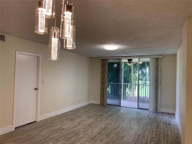 An empty room features wood-look flooring, a modern pendant light fixture, and a sliding glass door — 250 Jacaranda Drive # 203, Plantation FL 33324, PLANTATION, FL