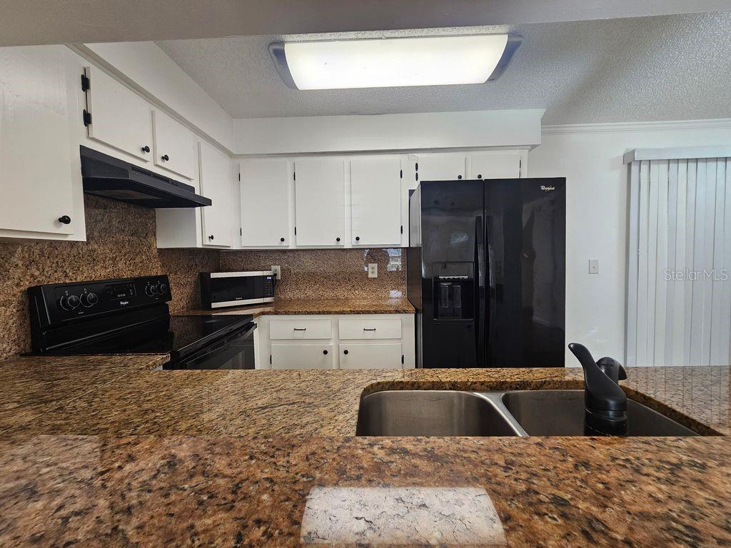 A kitchen features white cabinets, granite countertops, and black appliances with a double-basin sink — 601 BAINBRIDGE DRIVE, BRANDON, FL