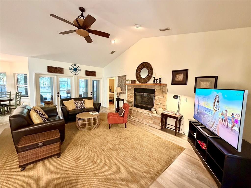 A living room features a stone fireplace, a large television, and a ceiling fan — 1043 SE COUNTY ROAD 21B, MELROSE, FL