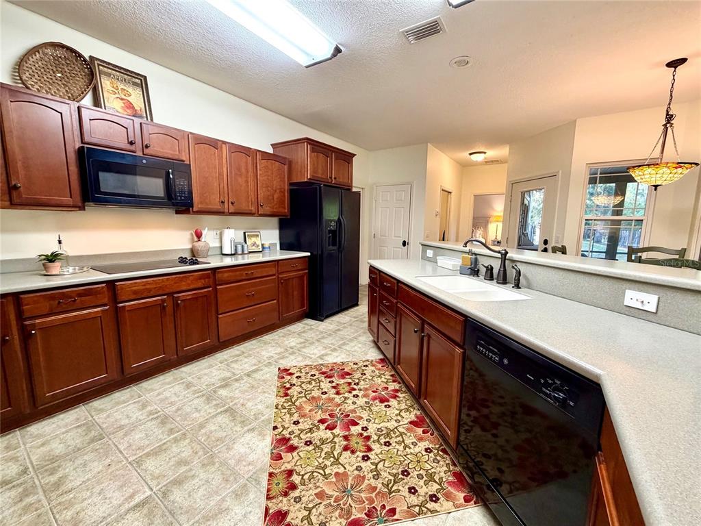 A kitchen features wood cabinets, black appliances, a central island with a sink, and tile flooring — 1043 SE COUNTY ROAD 21B, MELROSE, FL