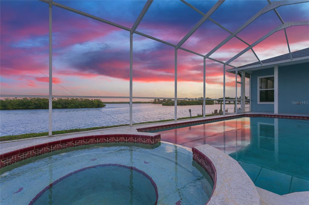 A screened-in pool and spa overlook a body of water at sunset — 5557 BOWLINE BEND, NEW PORT RICHEY, FL