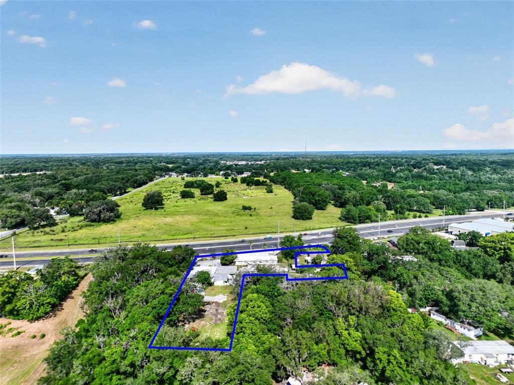 An aerial view shows a property outlined in blue, situated near a highway and trees — 1945 S US HIGHWAY 441, LADY LAKE, FL