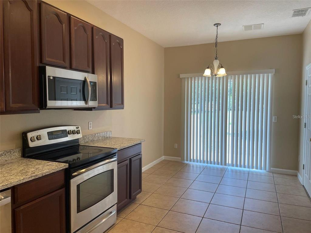 A kitchen with dark wood cabinets, stainless steel appliances, granite countertops, and tile flooring — 10303 PARK COMMONS DRIVE, ORLANDO, FL