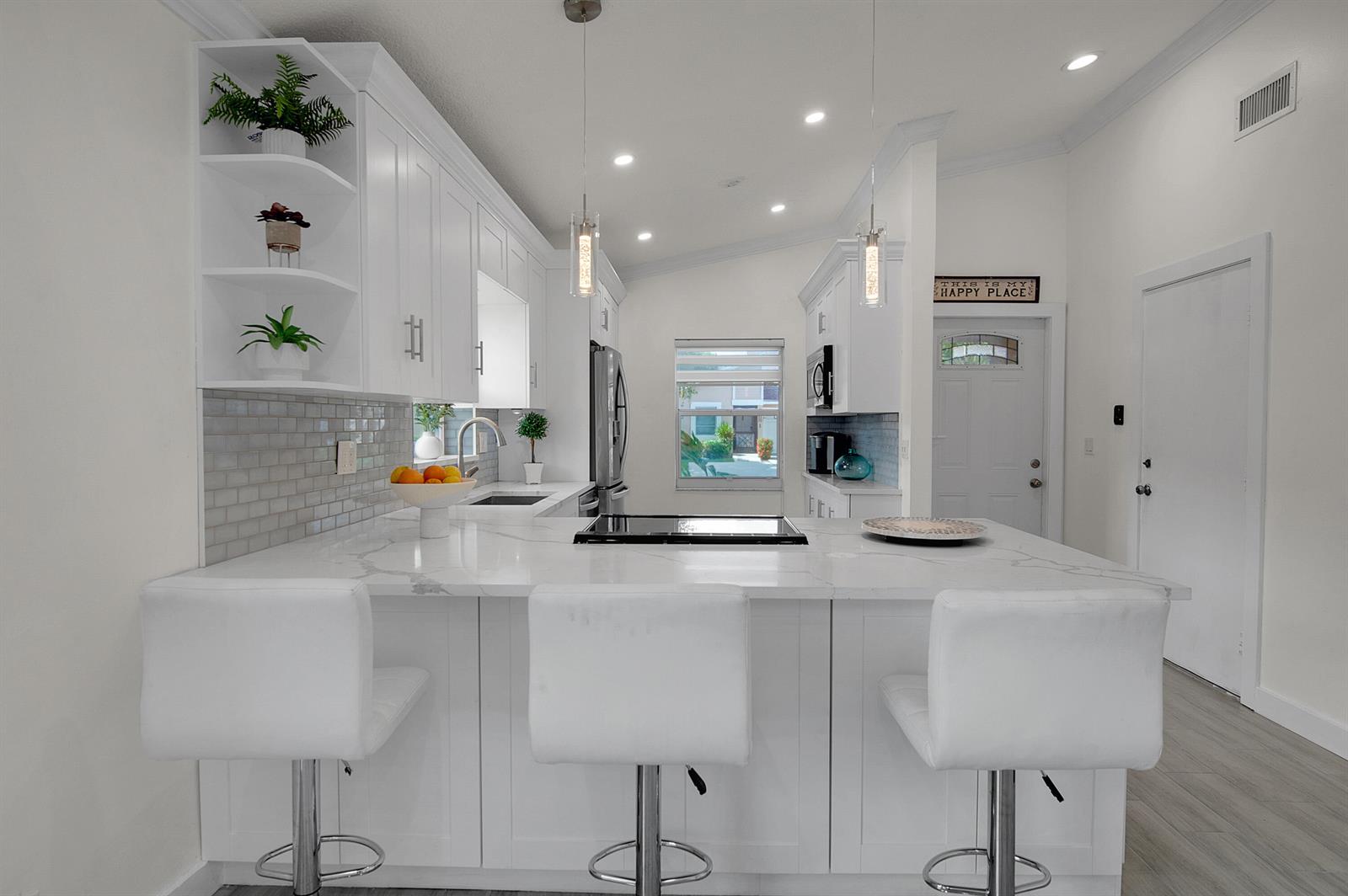 A modern white kitchen features a marble-topped island with three bar stools and pendant lighting — 8182 Springtree Road, Boca Raton FL 33496, BOCA RATON, FL