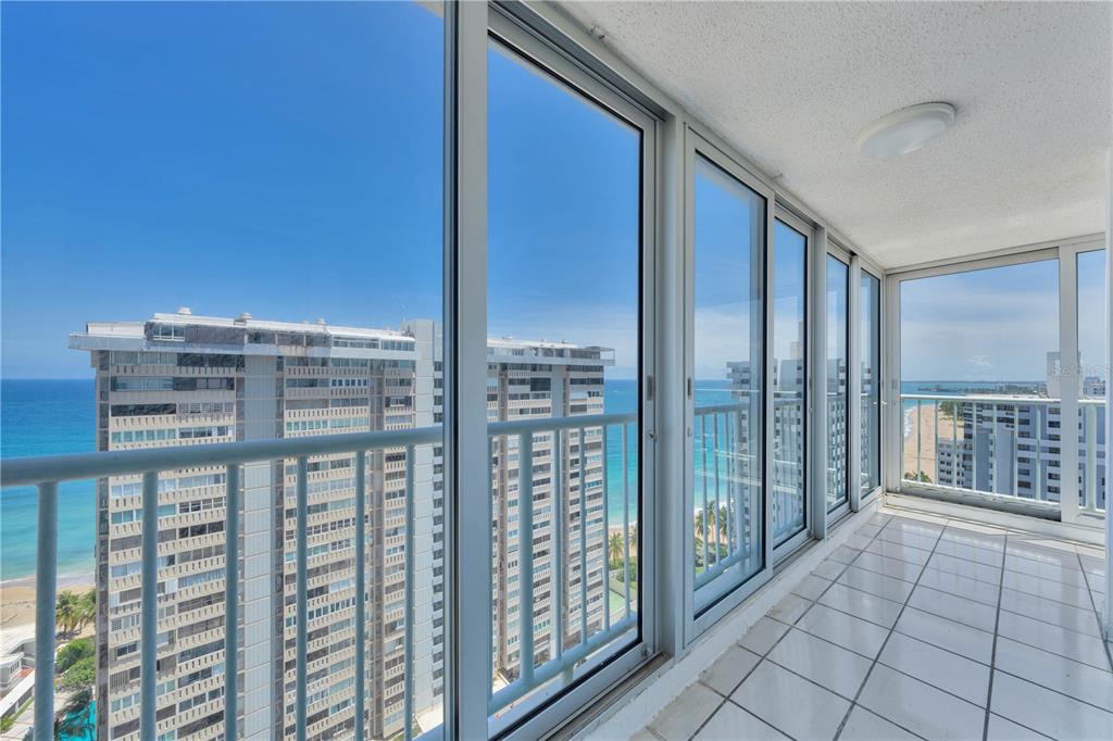 A sunroom with white tile floors and floor-to-ceiling windows overlooking the ocean and buildings — 1477 ASHFORD AVENUE UNIT 2206, SAN JUAN, PR