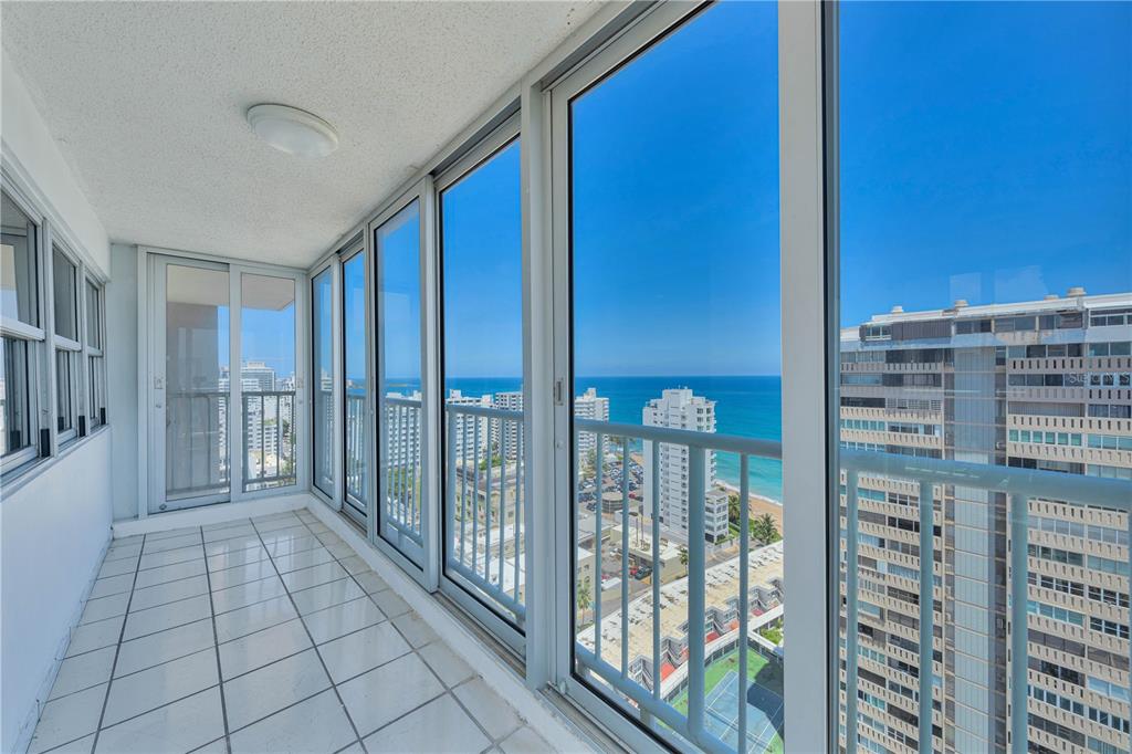 A tiled balcony with floor-to-ceiling windows overlooking the ocean and surrounding high-rise buildings — 1477 ASHFORD AVENUE UNIT 2206, SAN JUAN, PR