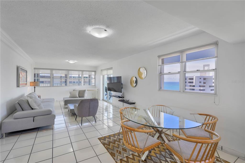 A bright living and dining area with white tile floors, a glass table, and ocean views — 1477 ASHFORD AVENUE UNIT 2206, SAN JUAN, PR