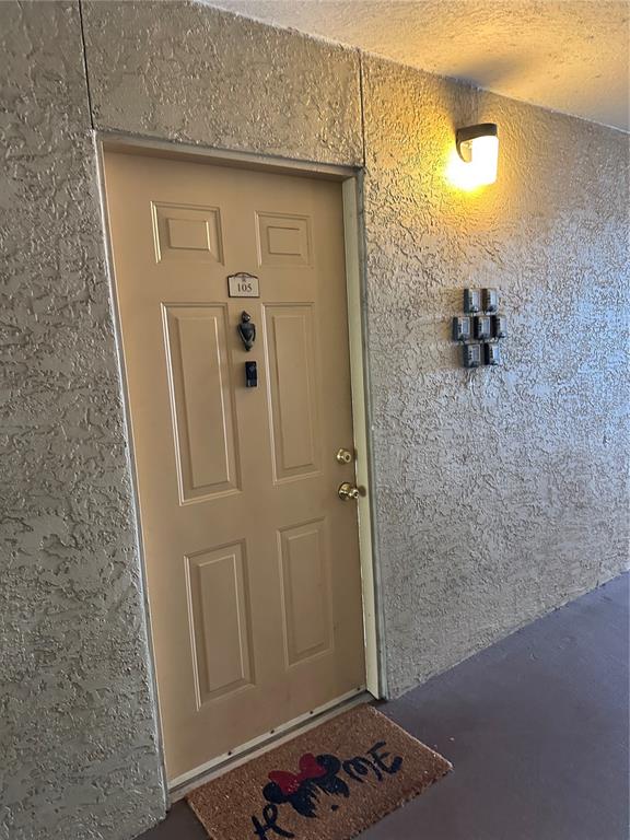 A tan apartment door numbered 105 features a Minnie Mouse doormat and several wall-mounted lockboxes — 822 CAMARGO WAY UNIT 105, ALTAMONTE SPRINGS, FL