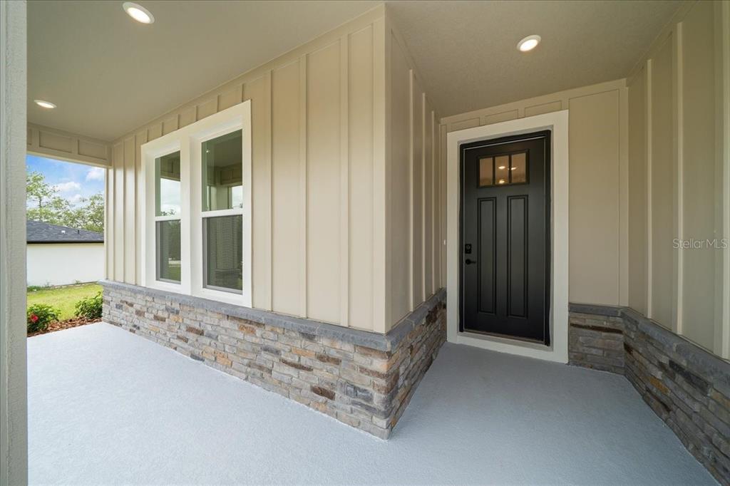 A covered front porch features board and batten siding, stone veneer, and a black door — 15095 SNOWY OWL AVENUE, WEEKI WACHEE, FL