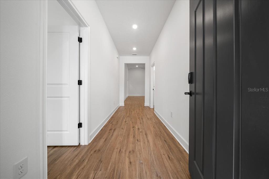 A hallway with light wood-look flooring leads to an open room with white walls — 15095 SNOWY OWL AVENUE, WEEKI WACHEE, FL