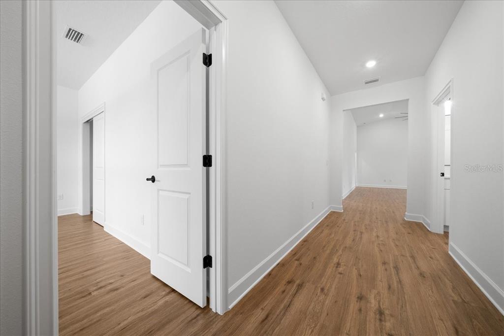 A hallway with light wood-look flooring leads to an open room with white walls — 15095 SNOWY OWL AVENUE, WEEKI WACHEE, FL