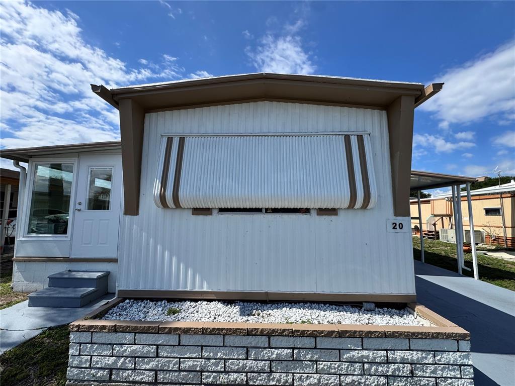 The exterior of a white mobile home features a metal awning and a brick planter — 420 49TH STREET E UNIT 20, PALMETTO, FL