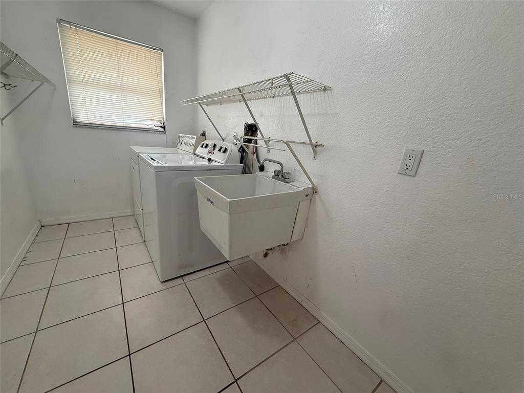 A laundry room features a white utility sink, a washing machine, and wire shelving — 1001 S WAPELLO STREET, NORTH PORT, FL