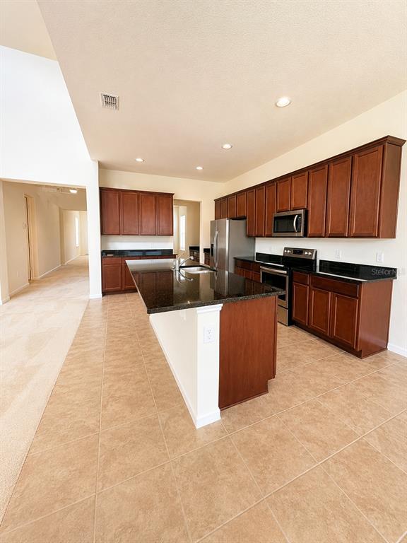 A kitchen features dark wood cabinets, granite countertops, an island, and tile flooring — 10103 AUSTRINA OAK LOOP, WINTER GARDEN, FL