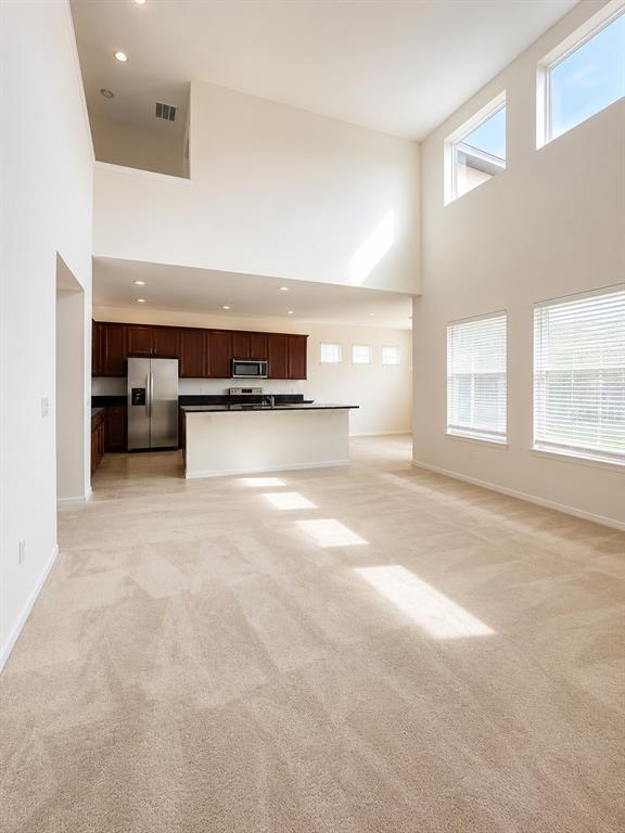 A spacious living room with high ceilings and carpeted floors opens to a kitchen area — 10103 AUSTRINA OAK LOOP, WINTER GARDEN, FL