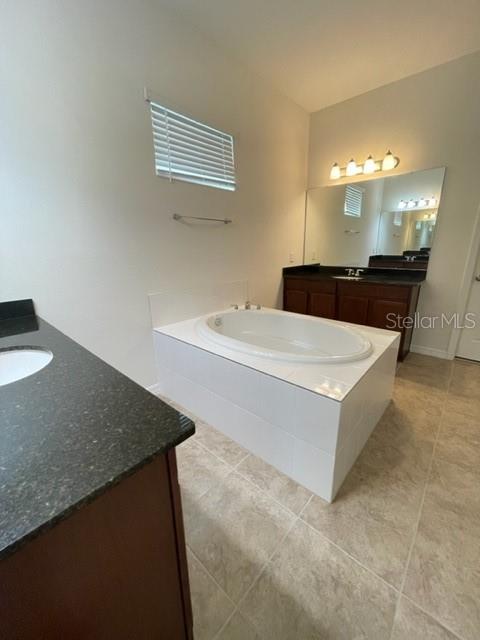 A bathroom features a tiled soaking tub, a dark vanity with a mirror, and tile flooring — 10103 AUSTRINA OAK LOOP, WINTER GARDEN, FL