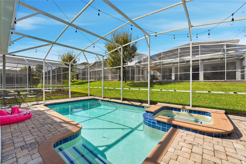 A screened-in swimming pool and spa with a brick paver deck and grassy backyard — 1584 SANDBAGGER DRIVE, DAVENPORT, FL
