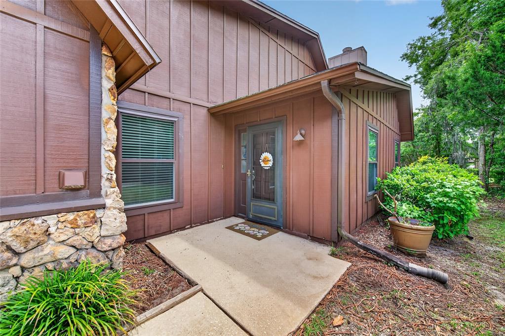 A brown wood-sided house features a stone accent wall, a concrete entryway, and a door — 8 MIMOSA TRAIL, ORMOND BEACH, FL