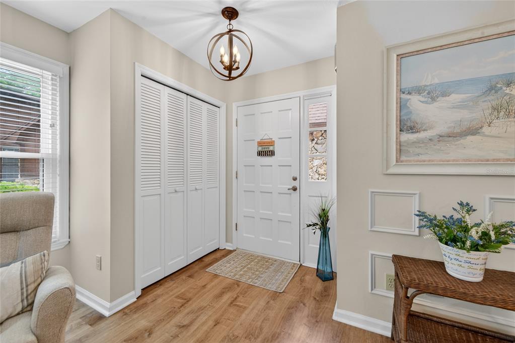 An entryway features wood-look flooring, a white paneled door, louvered closet doors, and a chandelier — 8 MIMOSA TRAIL, ORMOND BEACH, FL