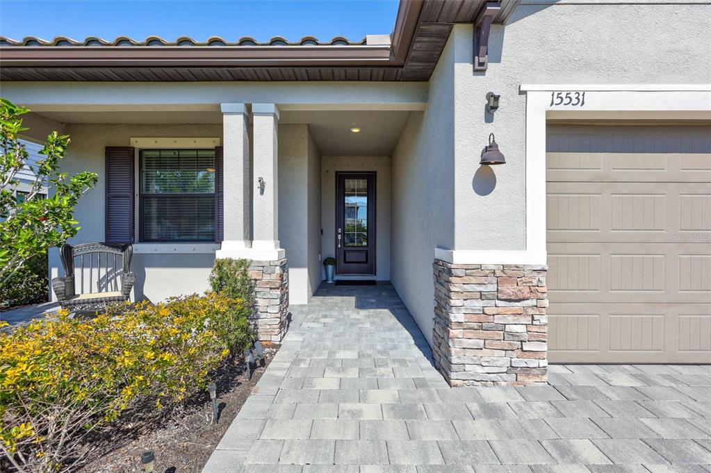 A paved walkway leads to the front entrance of a house with stone accents — 15531 ISLANDWALK AVENUE, LAKEWOOD RANCH, FL