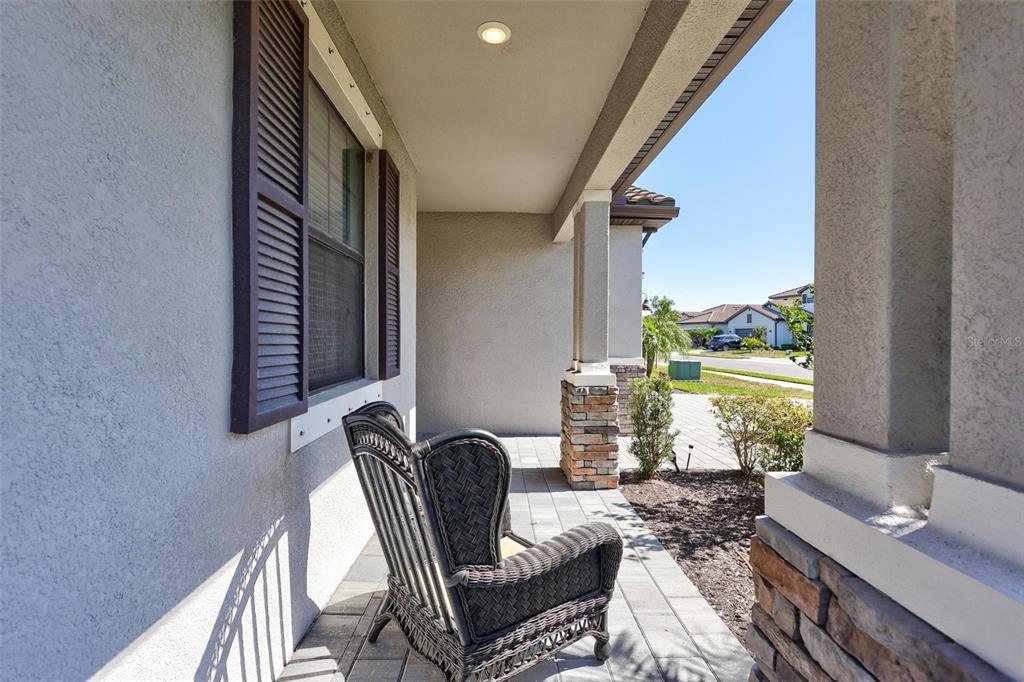 A covered front porch features a wicker chair, stone-based columns, and a paved floor — 15531 ISLANDWALK AVENUE, LAKEWOOD RANCH, FL