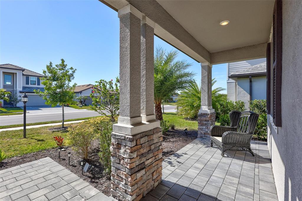 A covered front porch features stone-based columns, gray paver flooring, and two wicker chairs — 15531 ISLANDWALK AVENUE, LAKEWOOD RANCH, FL