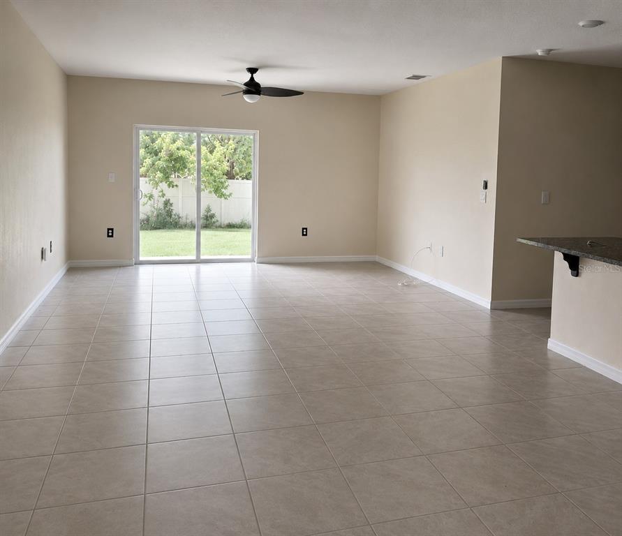 A spacious living room features light tile flooring, beige walls, a ceiling fan, and sliding doors — 2450 TALONCREST COURT, EAGLE LAKE, FL