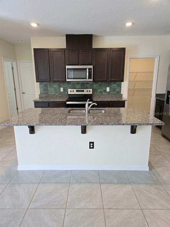 A kitchen features dark wood cabinets, granite countertops, a central island, and green tile backsplash — 2450 TALONCREST COURT, EAGLE LAKE, FL