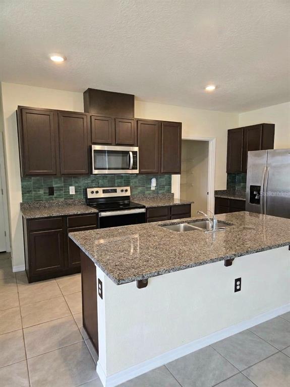 A kitchen features dark wood cabinets, granite countertops, a kitchen island, and stainless steel appliances — 2450 TALONCREST COURT, EAGLE LAKE, FL