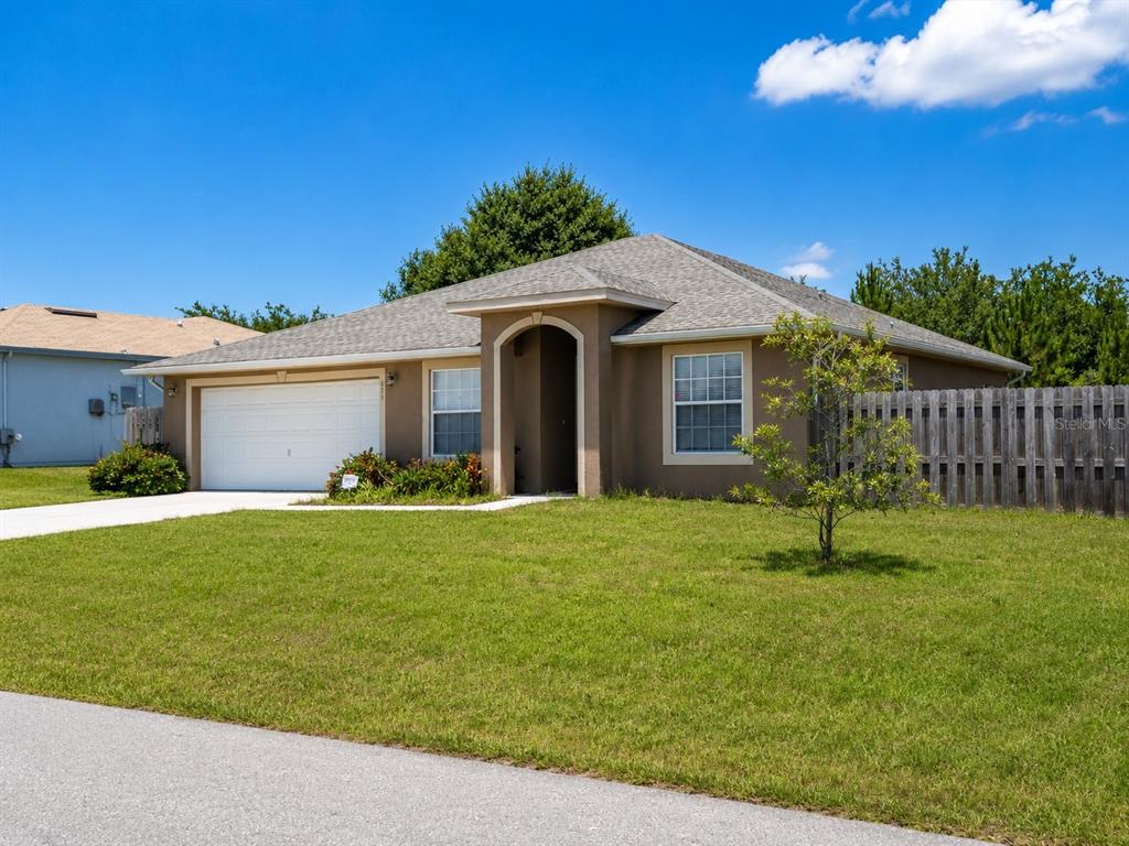 A single-story tan house with a two-car garage and a wooden fence in the yard — 101 BONITO WAY, POINCIANA, FL