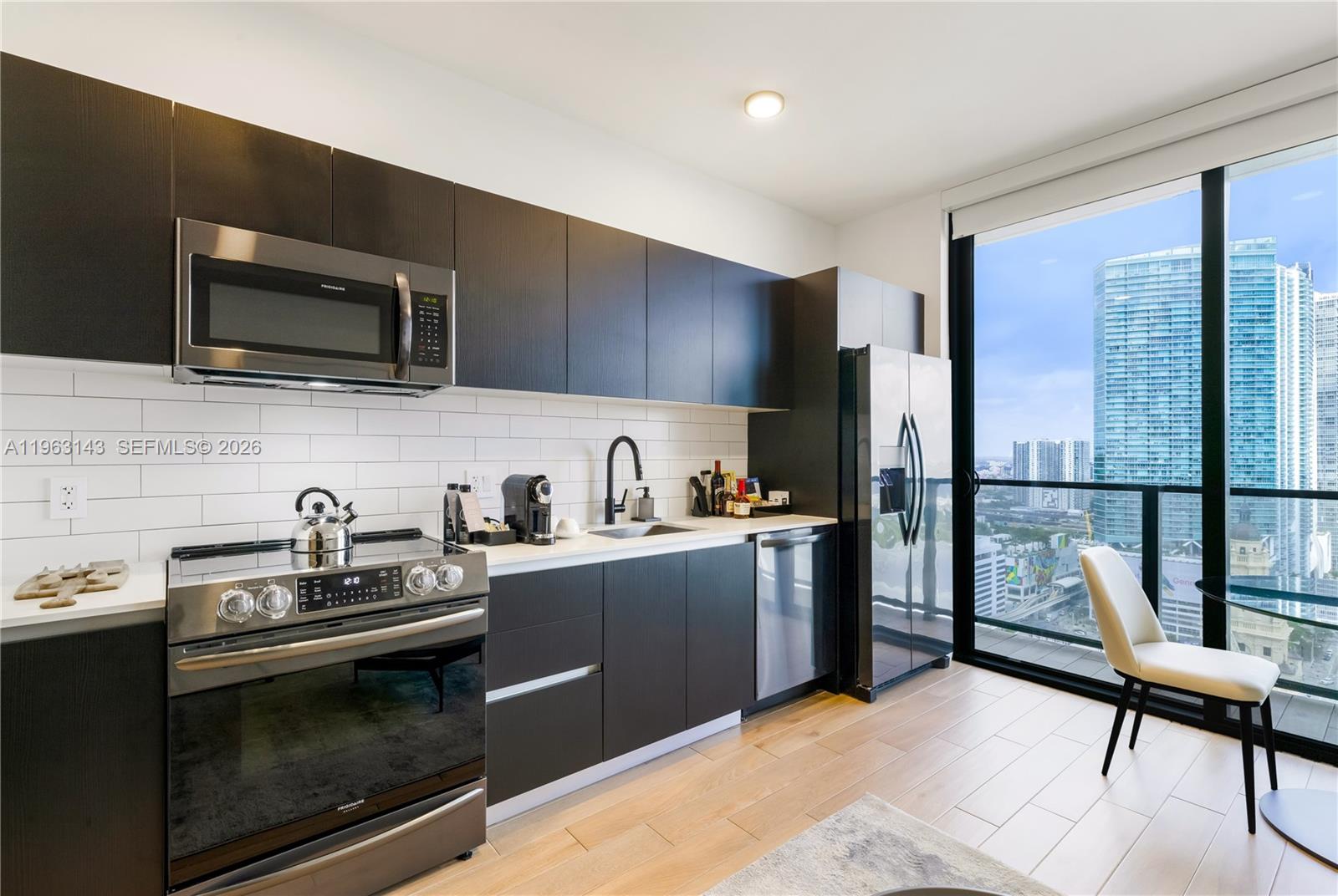 A modern kitchen features dark cabinetry, stainless steel appliances, and a view of city skyscrapers — 398 NE 5th St # 2205, Miami FL 33132, MIAMI, FL