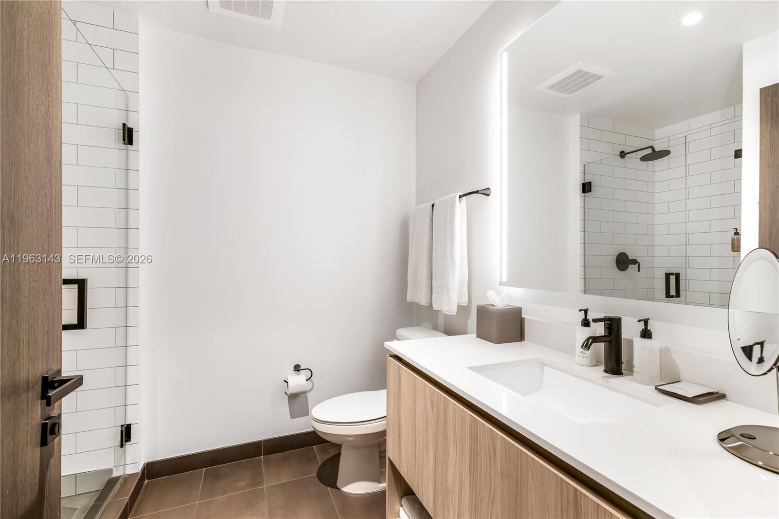A modern bathroom features a wood vanity, white subway tile shower, and a backlit mirror — 398 NE 5th St # 2205, Miami FL 33132, MIAMI, FL