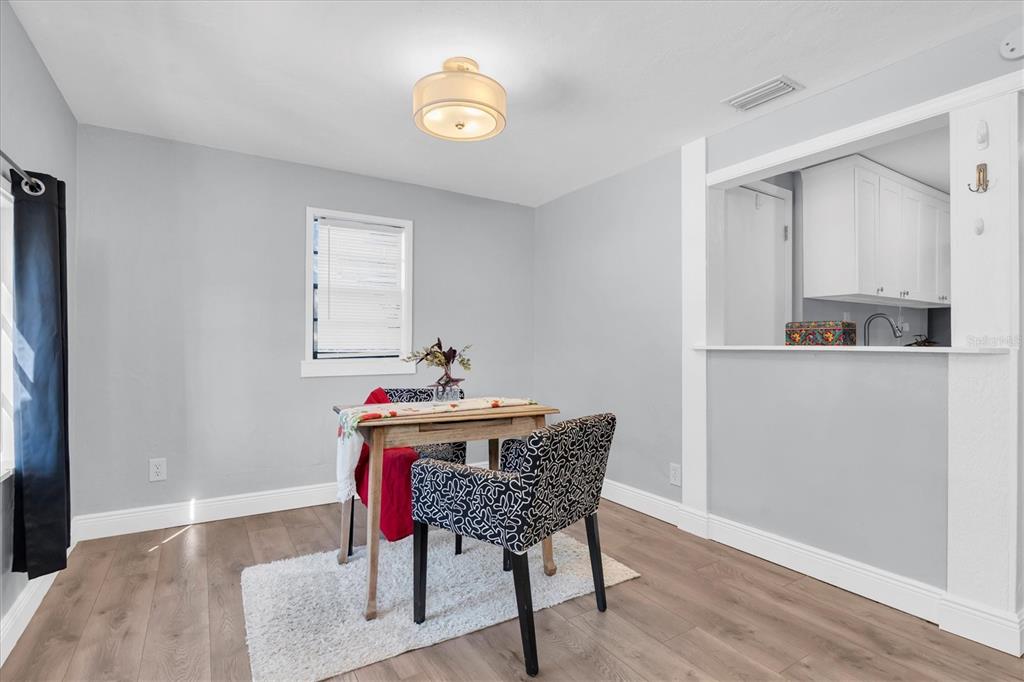 A dining area features light gray walls, wood-look flooring, a small table, and a kitchen pass-through — 5107 37TH STREET N, ST PETERSBURG, FL