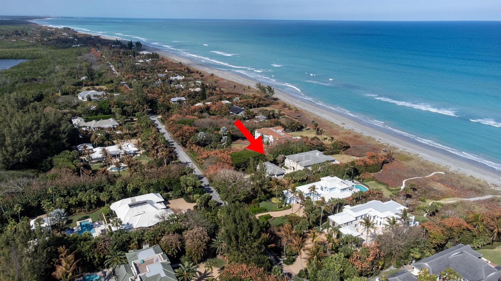 An aerial view shows a coastal neighborhood with houses nestled among trees near the ocean — 19 N Beach Road, Jupiter Island FL 33455, JUPITER ISLAND, FL