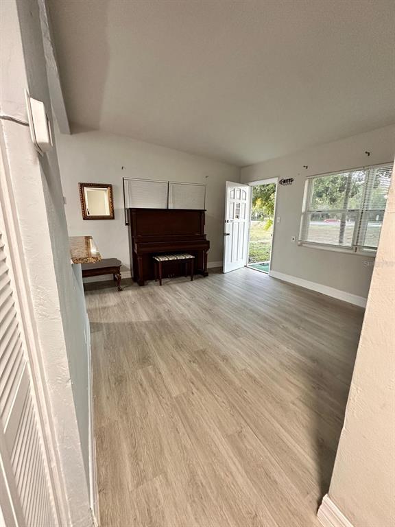 A living room with light wood-look flooring, a piano, and an open exterior door — 3508 ORANOLE ROAD, ORLANDO, FL