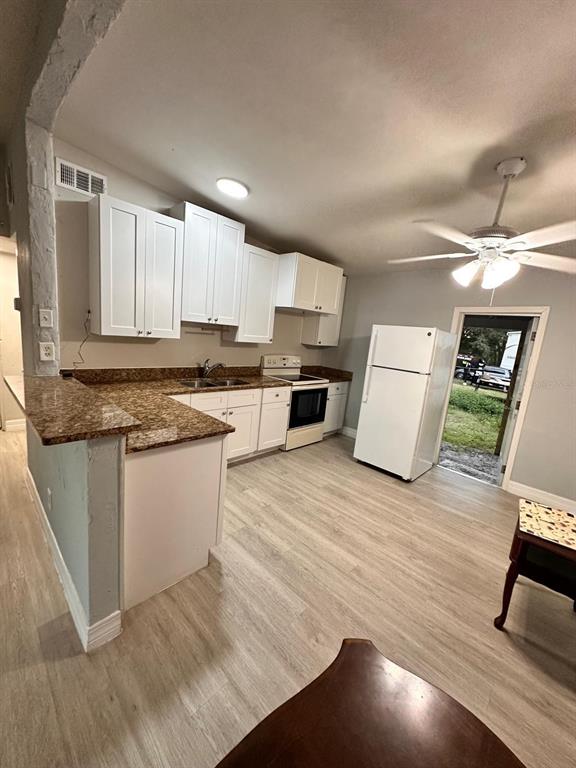 A kitchen features white cabinets, granite countertops, light wood-look flooring, and a ceiling fan — 3508 ORANOLE ROAD, ORLANDO, FL
