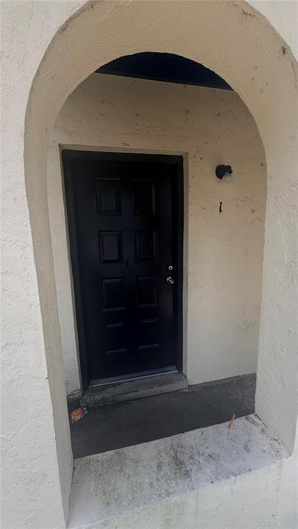 A black front door is set within a recessed arched entryway of a stucco building — 2735 SW 35TH PLACE UNIT 1801, GAINESVILLE, FL