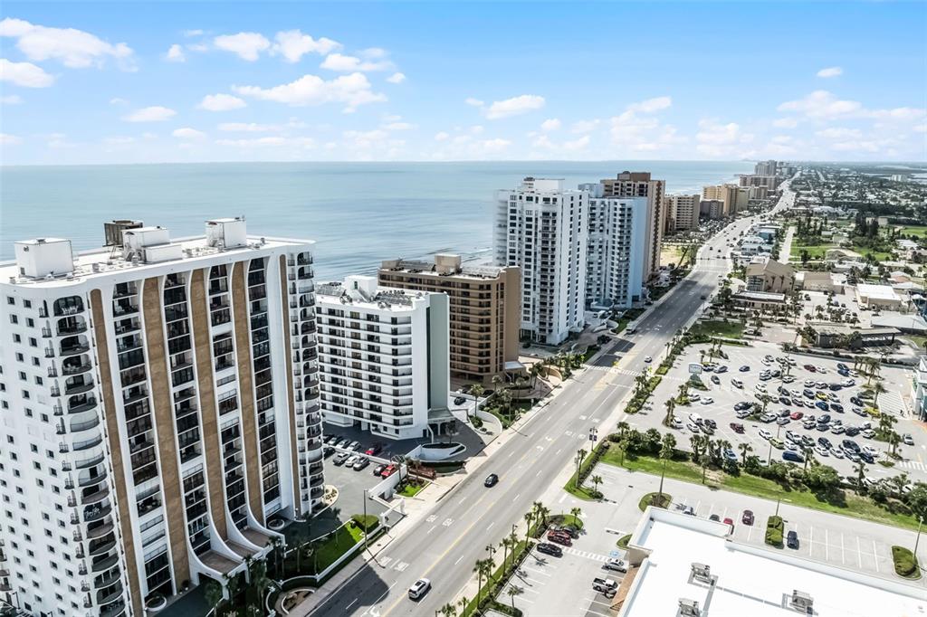 An aerial view shows high-rise oceanfront buildings along a coastal road with a parking lot — 3023 S ATLANTIC AVENUE UNIT 6060, DAYTONA BEACH, FL