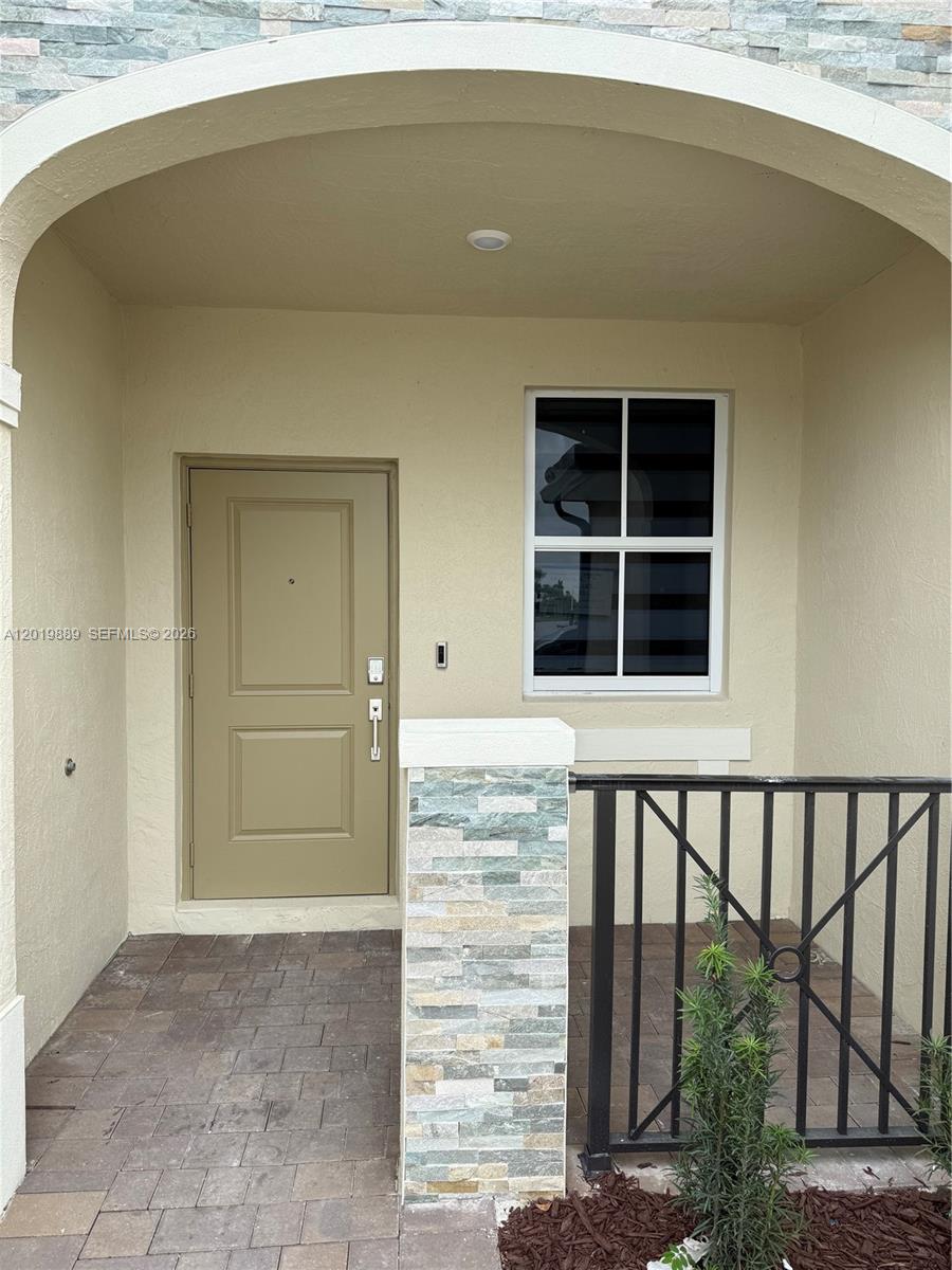 A covered entryway features a tan door, a single window, and a stone-accented pillar — HOMESTEAD, FL