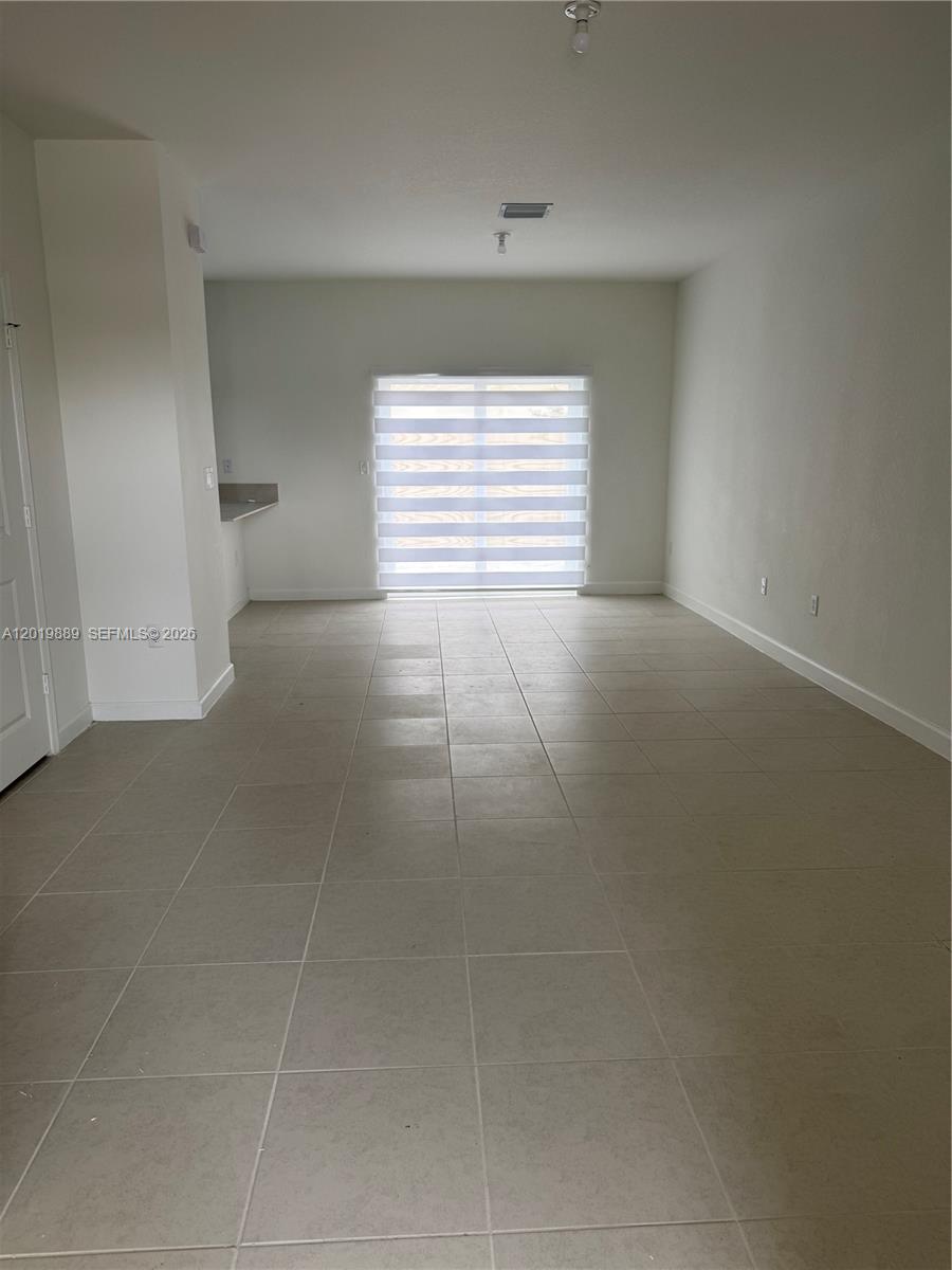 An empty room features light-colored tile flooring, white walls, and a sliding glass door — HOMESTEAD, FL