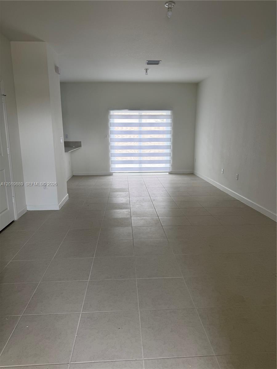 An empty room features light-colored tile flooring, white walls, and a sliding glass door — HOMESTEAD, FL