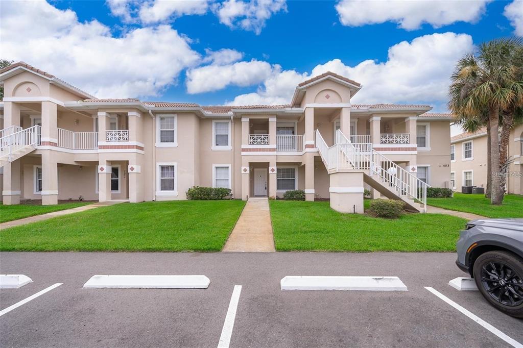 A two-story apartment building with beige stucco walls, white railings, and a parking lot — 13403 FAIRWAY GLEN DRIVE UNIT 203, ORLANDO, FL