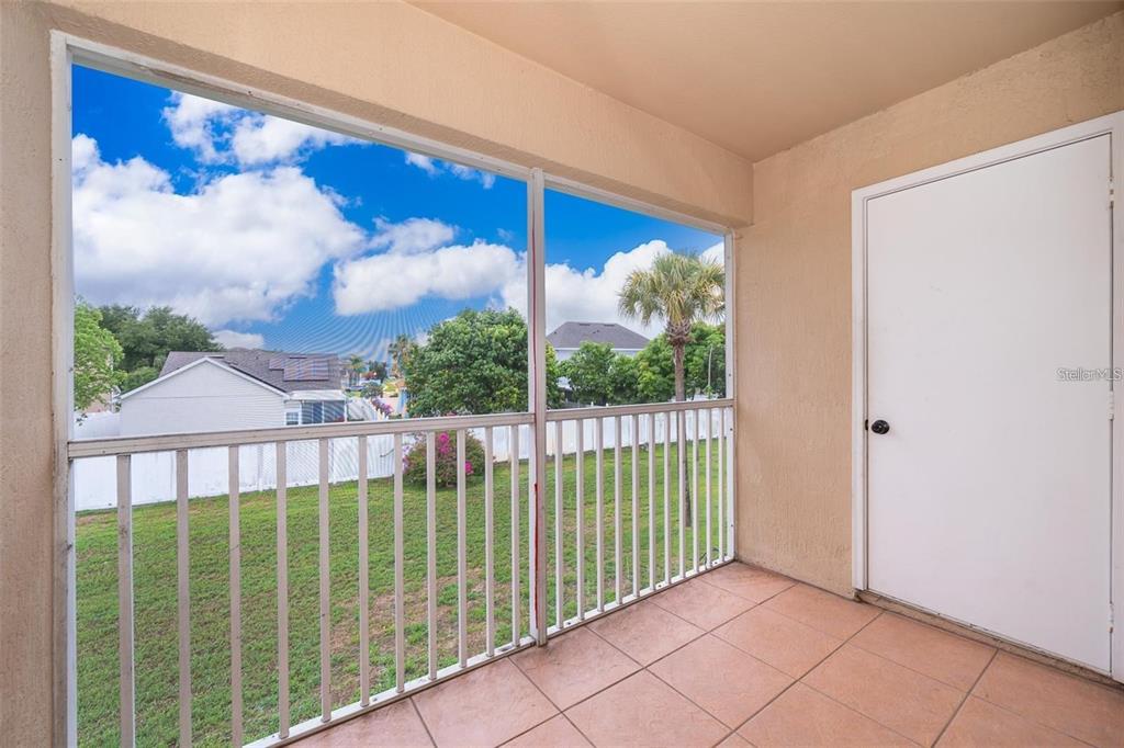 A screened-in balcony with tiled flooring overlooks a grassy yard and neighboring houses — 13403 FAIRWAY GLEN DRIVE UNIT 203, ORLANDO, FL