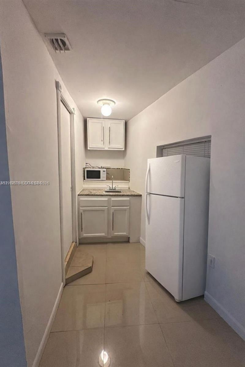A small kitchen features white cabinets, a granite countertop, a sink, and a white refrigerator — 1572 NE 149th St # C, Miami FL 33161, MIAMI, FL