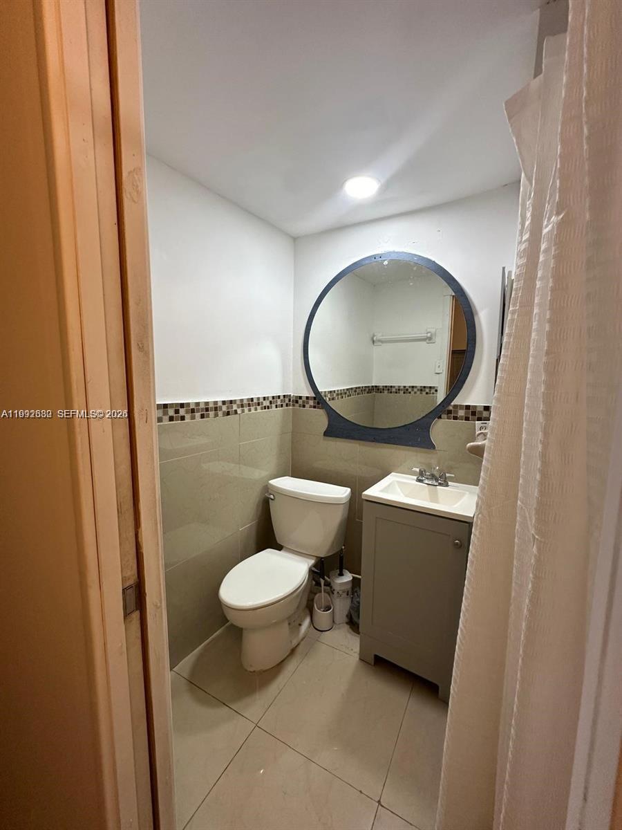 A small bathroom features a toilet, a vanity with a sink, and a round mirror — 1572 NE 149th St # C, Miami FL 33161, MIAMI, FL