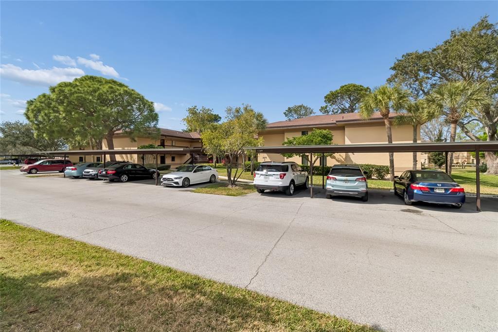 An exterior view of a multi-story apartment building with covered parking spaces and parked cars — 2679 SABAL SPRINGS CIRCLE UNIT 102, CLEARWATER, FL