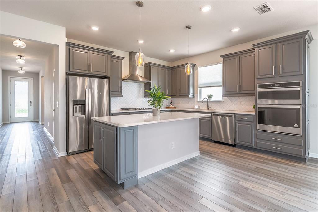 A modern kitchen features gray cabinets, stainless steel appliances, a center island, and wood flooring — 1681 BLOSSOM SOUND COURT, OVIEDO, FL