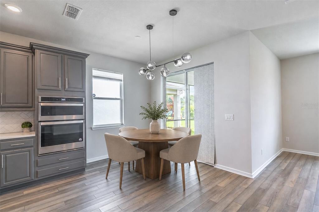 A dining area features a round wooden table, four chairs, and a modern globe chandelier — 1681 BLOSSOM SOUND COURT, OVIEDO, FL