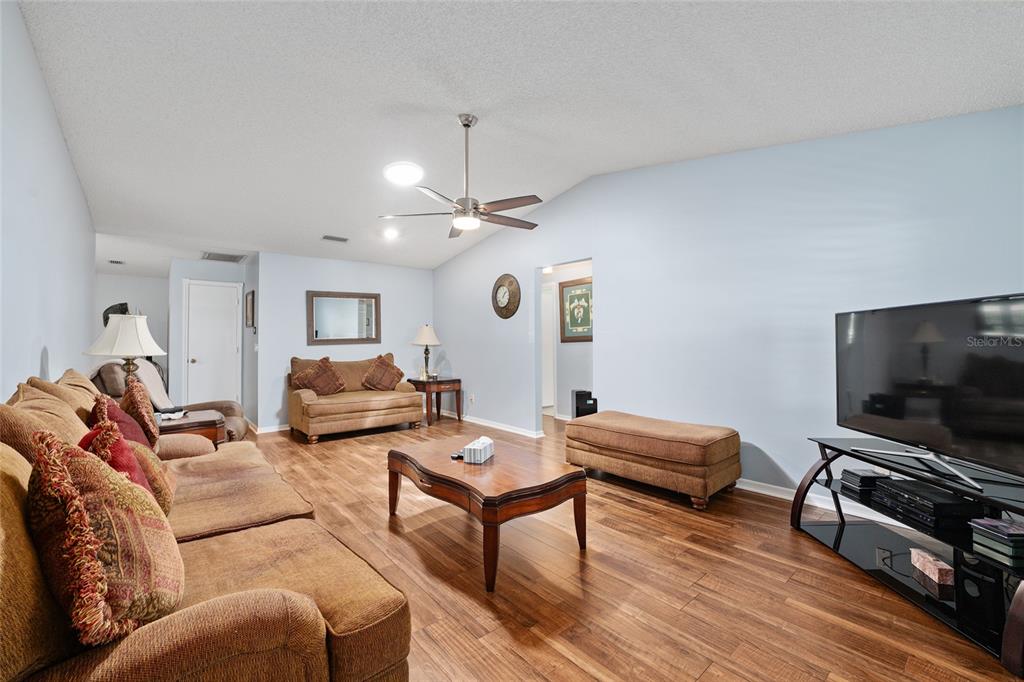 A living room features light blue walls, wood-look flooring, a ceiling fan, and brown furniture — 9820 SW 89TH TERRACE UNIT E, OCALA, FL