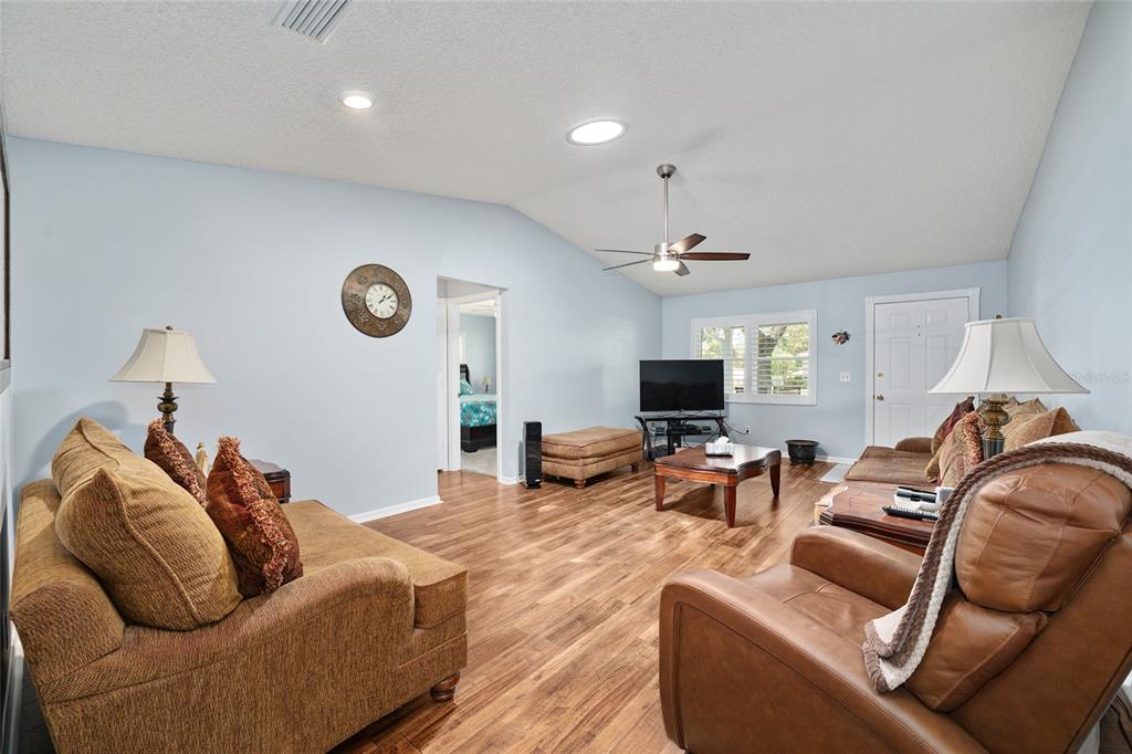 A living room features light blue walls, wood-look flooring, a vaulted ceiling, and brown furniture — 9820 SW 89TH TERRACE UNIT E, OCALA, FL